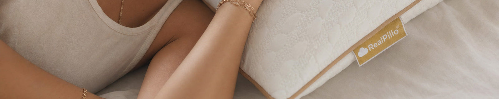 Banner of detail of a woman's arm and covered breast resting on a RealPillo® pillow with a visible golden label tag