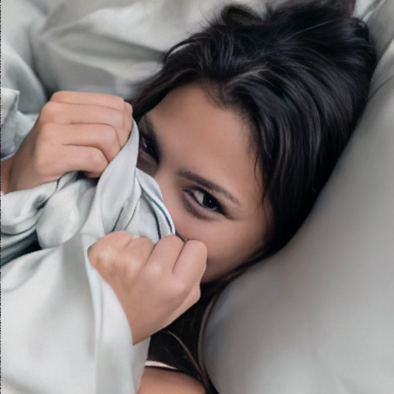 Woman peeking from under a Reallin® bedding sheet in Tencel® and Fairtrade® cotton on a bed