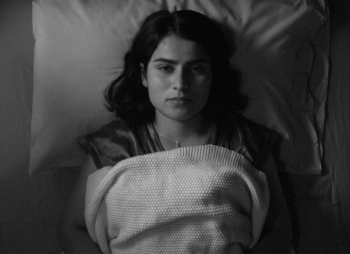 Woman lying in bed with a blanket, looking contemplative.