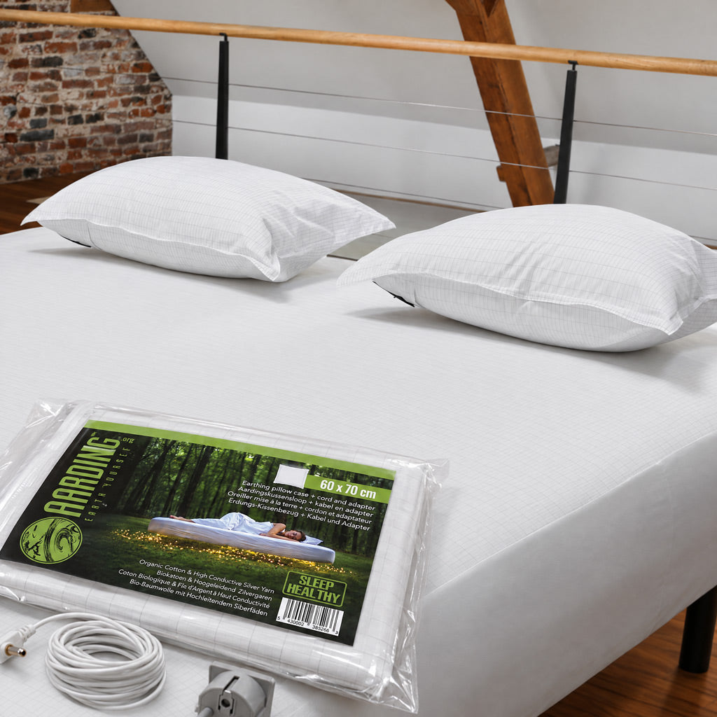 Two white grounding pillows with silver yarn, alongside its retail packaging and power cord. The brand 'Aarding' is visible on the packaging label.